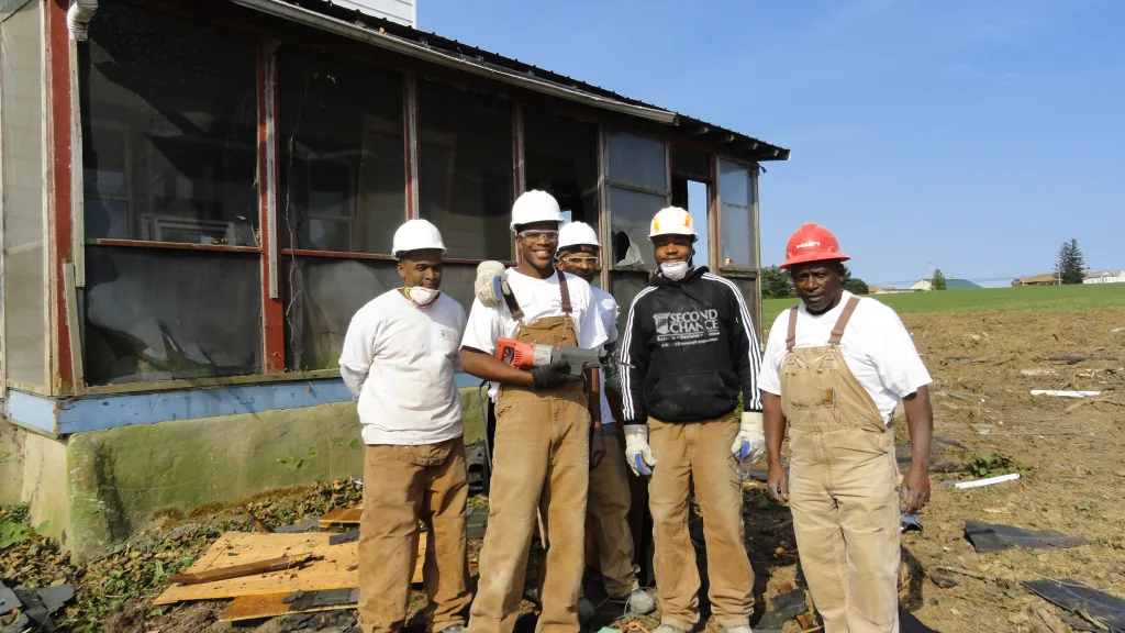 Second Chance Baltimore non-profit team of five workers in hard hats and overalls salvaging wood and used building materials from an old house. This deconstruction project recovers valuable, sustainable items for resale and community programs.