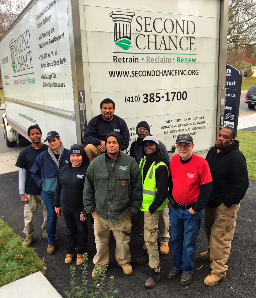 A diverse team from Second Chance, a Baltimore non-profit, stands proudly by their truck, ready to reclaim salvaged building materials, vintage furniture, and unique antique hardware for sustainable home improvement.