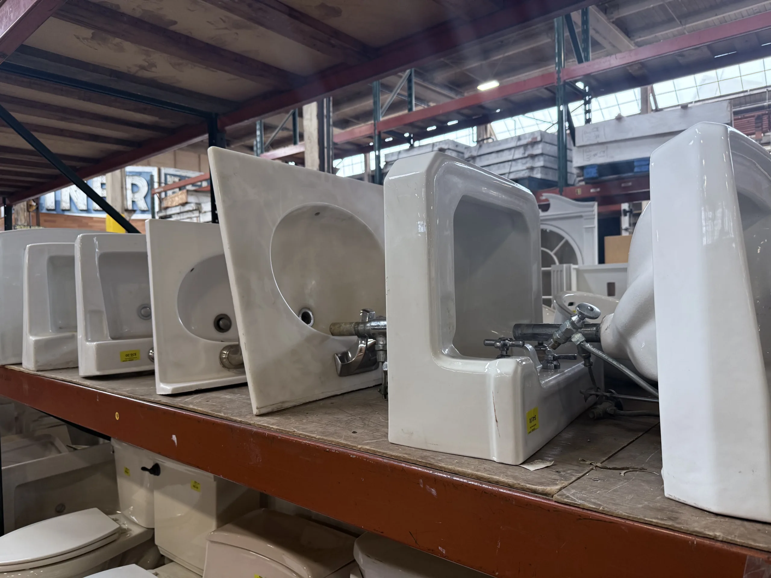 Salvaged white ceramic sinks and urinals displayed on shelving at Second Chance, Inc., a Baltimore non-profit. Find affordable secondhand plumbing fixtures and used building materials for home renovation.