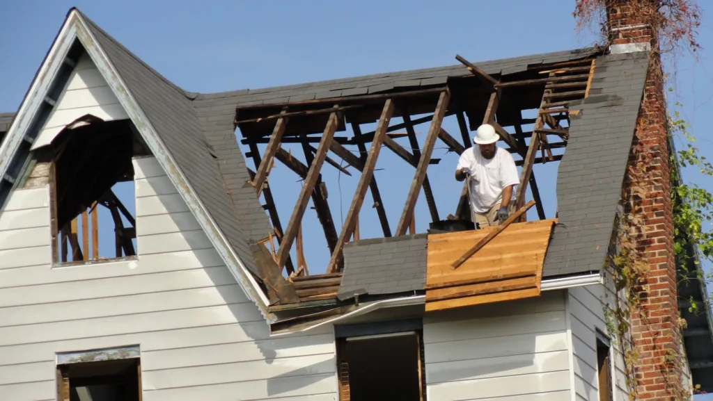 Worker on a deconstructed house roof salvaging valuable building materials like reclaimed wood and secondhand shingles. Second Chance, a Baltimore non-profit, collects these used building materials for sustainable home improvement and unique projects.