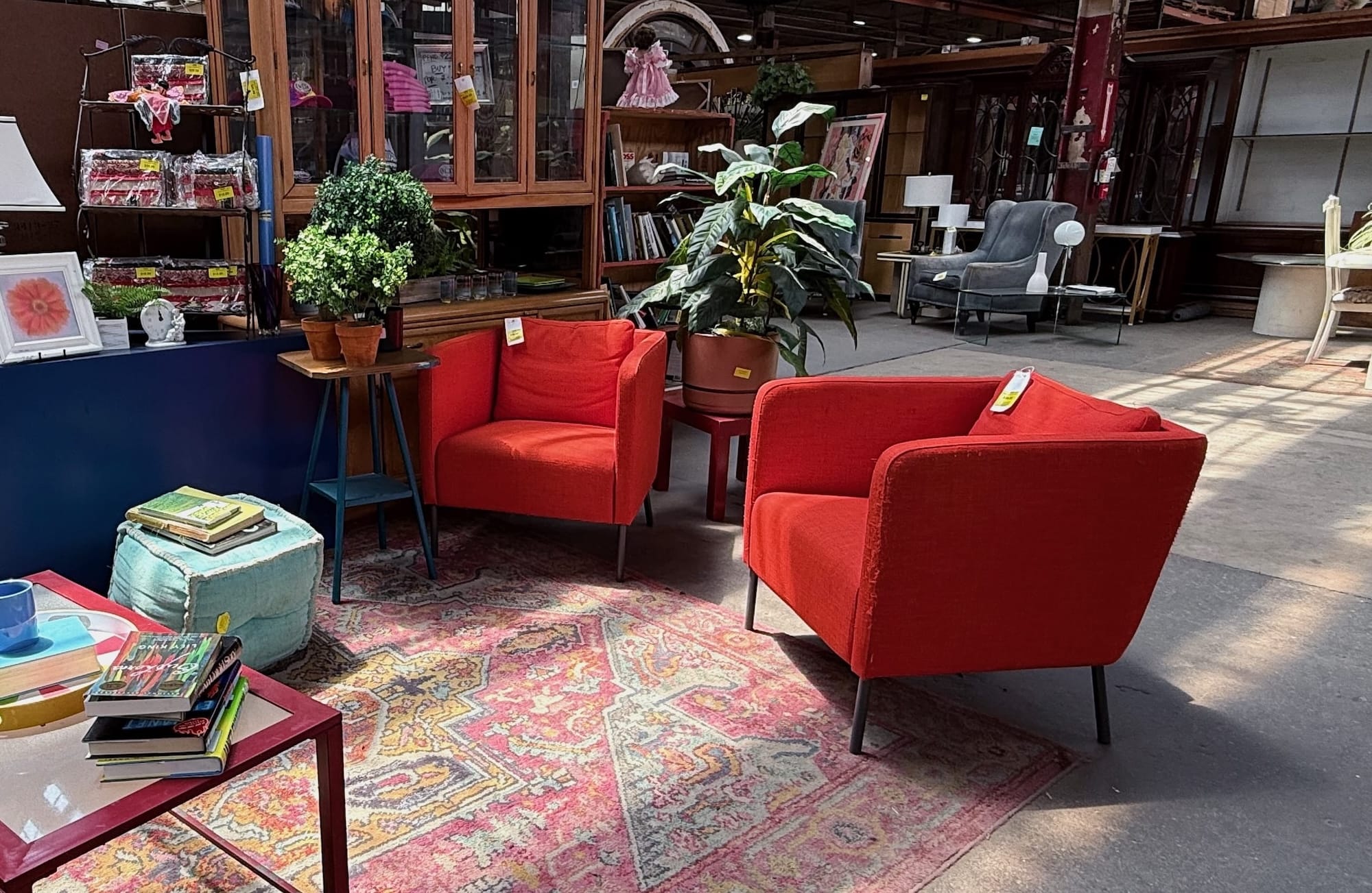 Showroom at Second Chance, a Baltimore non-profit, featuring two red secondhand armchairs on a patterned rug, surrounded by vintage furniture, lamps, and unique home decor items. Discover salvaged treasures and used building materials.