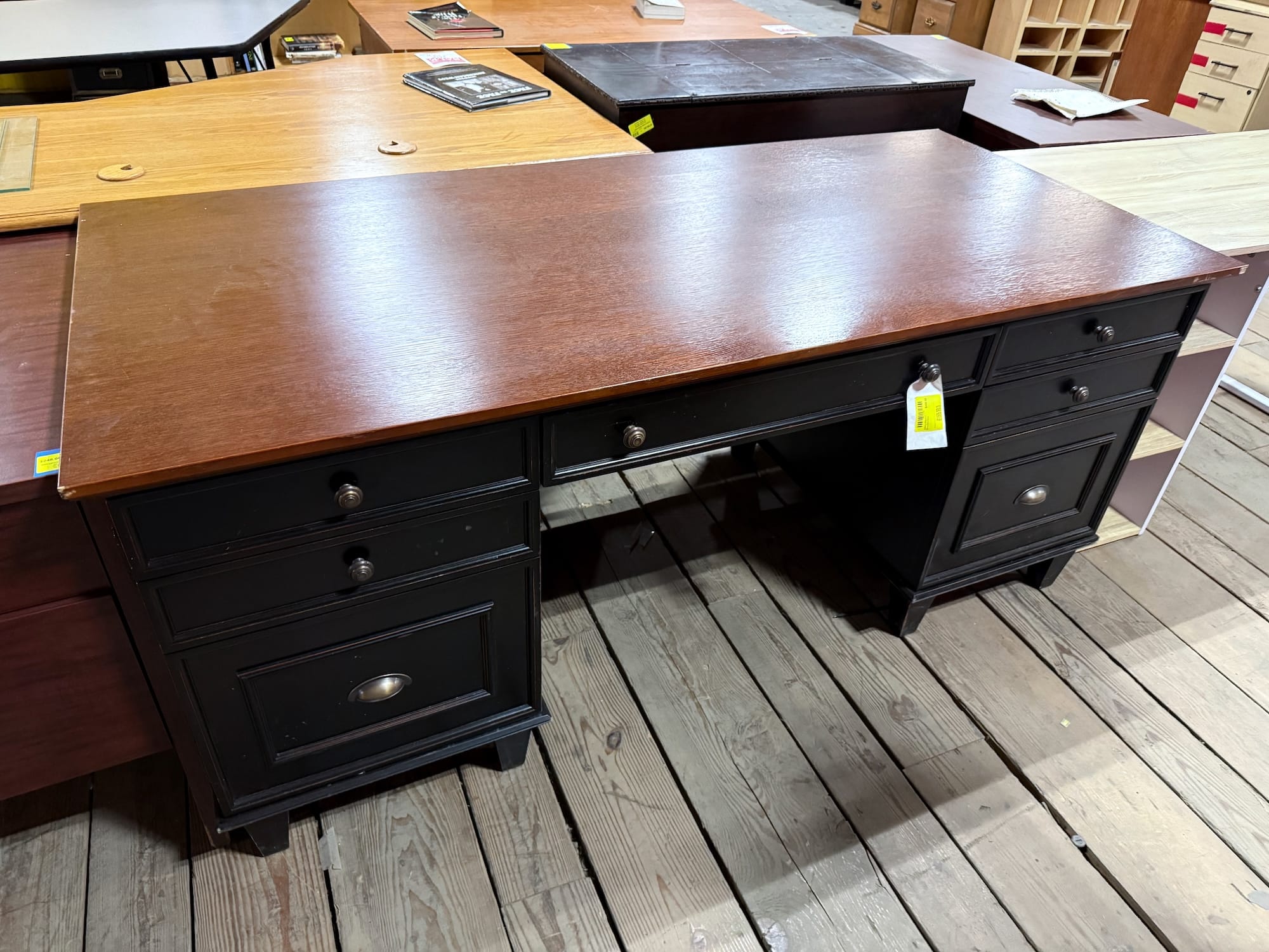 Vintage-style black desk with dark wood top and multiple drawers, featuring antique hardware pulls. This unique secondhand furniture piece is available from our Baltimore non-profit, offering salvaged home goods.